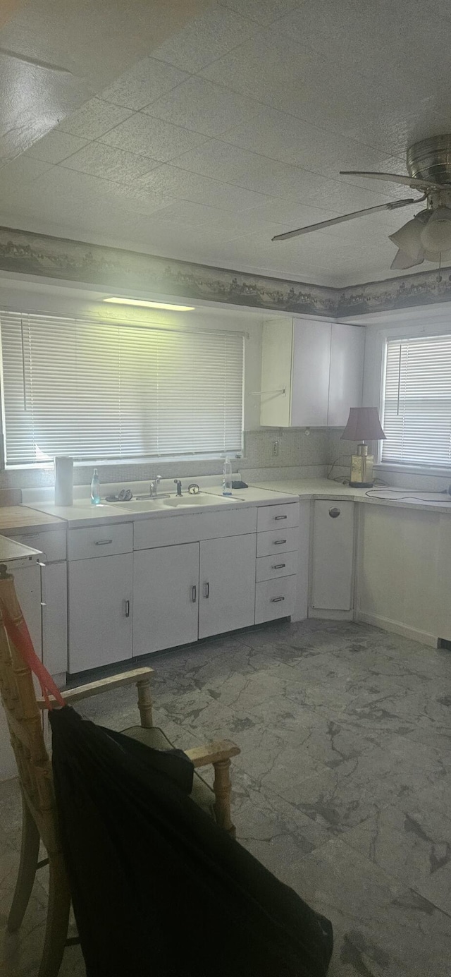 kitchen featuring light countertops, white cabinetry, ceiling fan, and a sink