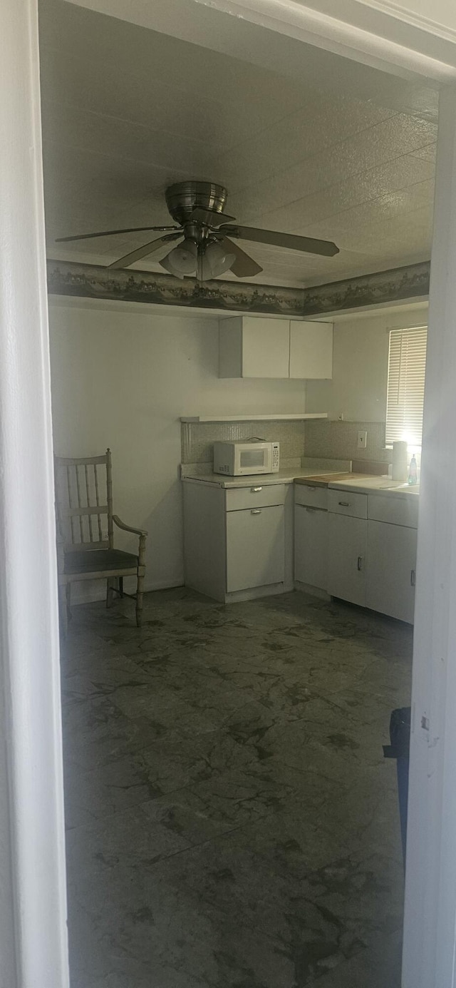kitchen featuring concrete floors, ceiling fan, white microwave, and white cabinets