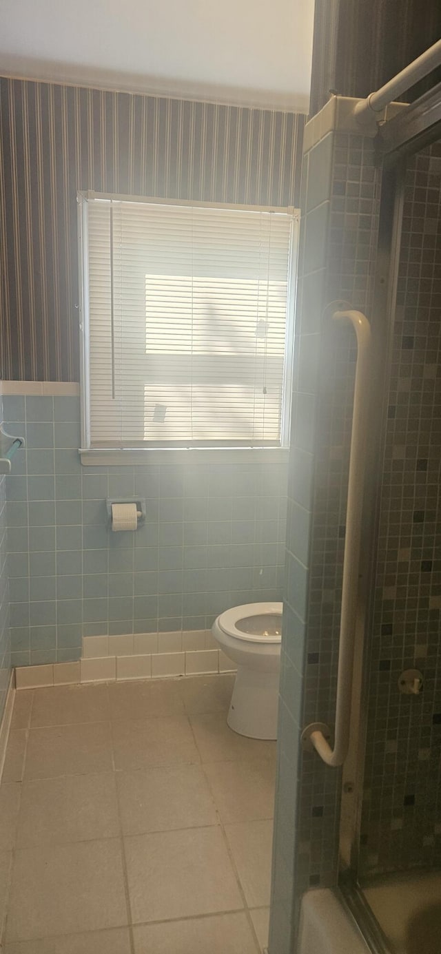 bathroom with tile walls, tile patterned flooring, a shower stall, toilet, and wallpapered walls