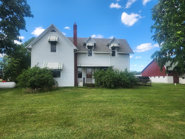 back of house featuring a chimney, a shingled roof, and a yard