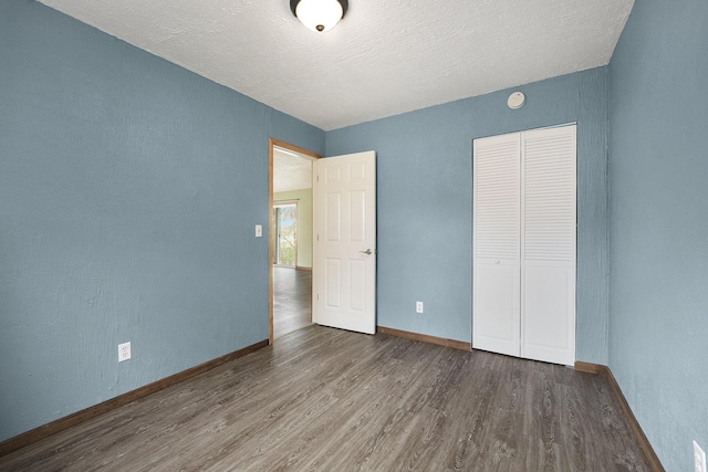 unfurnished bedroom featuring baseboards, wood finished floors, and a closet
