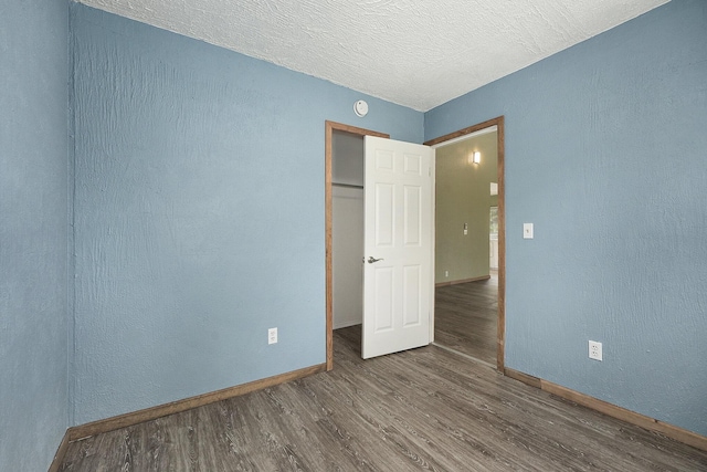 unfurnished bedroom with a textured ceiling, baseboards, a closet, and wood finished floors