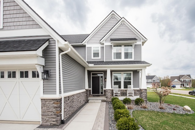 craftsman house with a garage, a front yard, covered porch, and stone siding