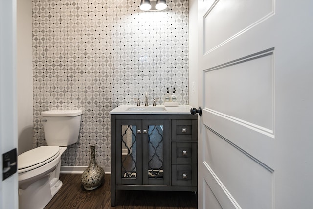half bath with baseboards, wood finished floors, toilet, and vanity