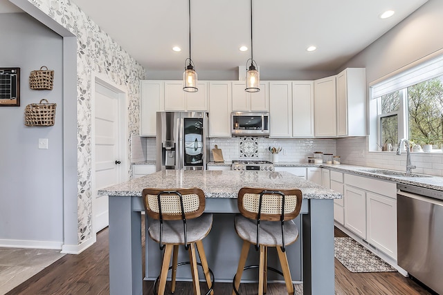 kitchen with light stone counters, a sink, a center island, stainless steel appliances, and baseboards