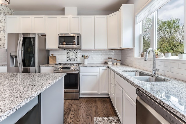 kitchen featuring light stone counters, a sink, white cabinets, and stainless steel appliances