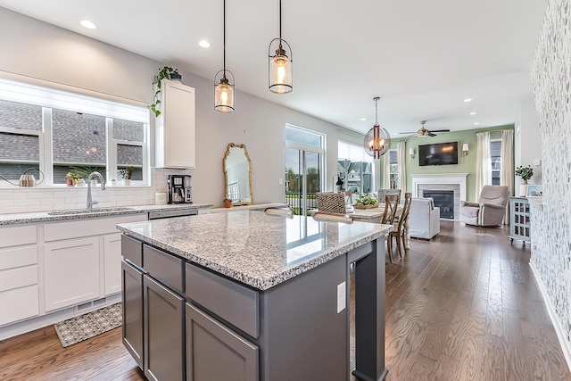 kitchen with a glass covered fireplace, gray cabinets, light stone counters, a sink, and dark wood finished floors