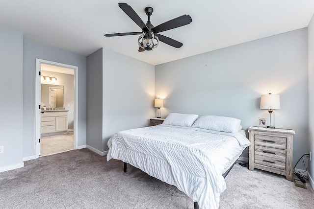 bedroom featuring a sink, light carpet, baseboards, ensuite bathroom, and a ceiling fan