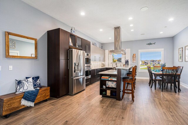 3080 Silver Fir Ct, Holland, MI 49424 - kitchen with appliances with stainless steel finishes, island range hood, light wood finished floors, dark brown cabinets, and a breakfast bar