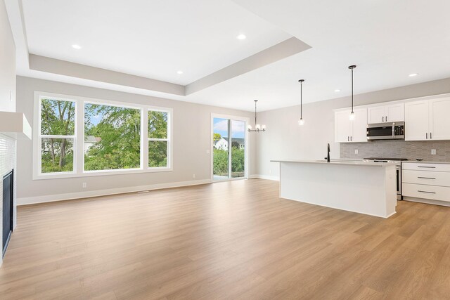 kitchen with an inviting chandelier, decorative backsplash, a glass covered fireplace, light wood finished floors, and stainless steel appliances