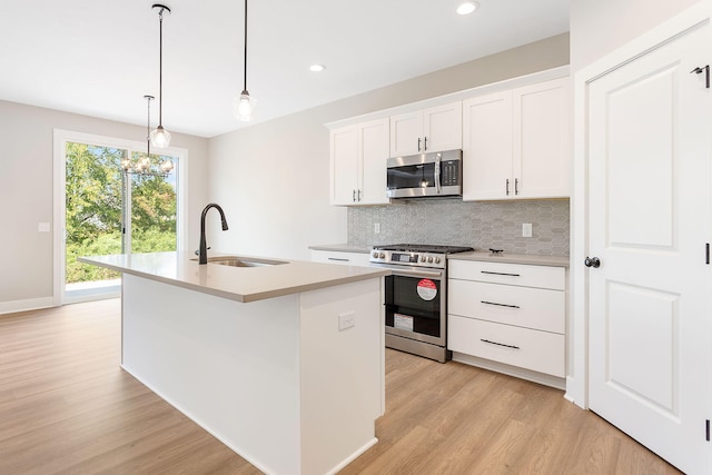 kitchen with an island with sink, light wood-type flooring, tasteful backsplash, a sink, and stainless steel appliances