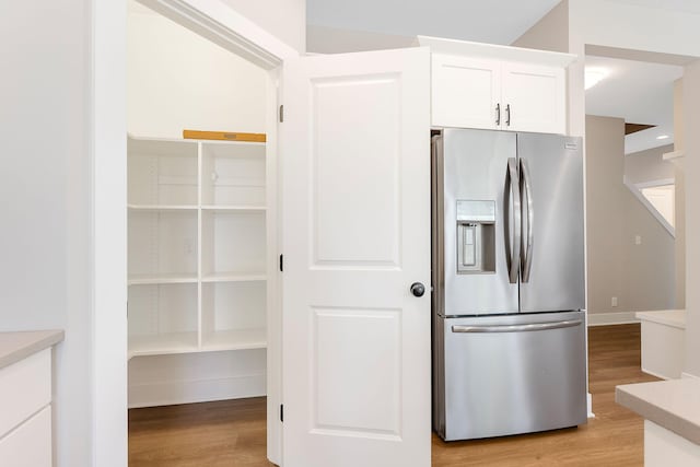 kitchen with stainless steel fridge, light countertops, white cabinets, and light wood-style floors