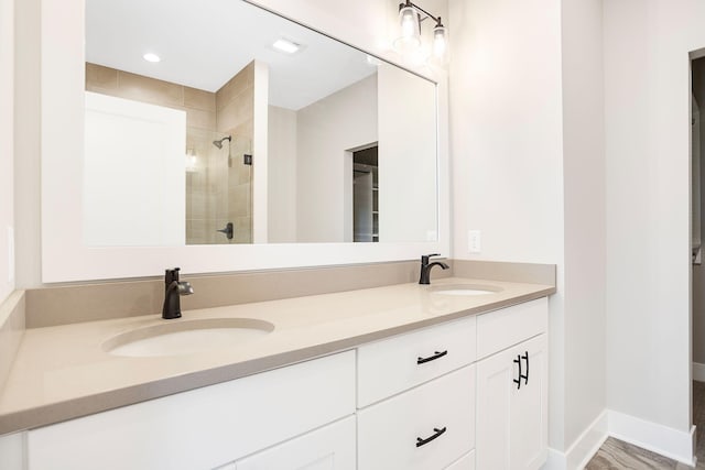 full bathroom with double vanity, baseboards, tiled shower, and a sink