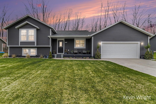 tri-level home with a shingled roof, a garage, concrete driveway, covered porch, and a yard