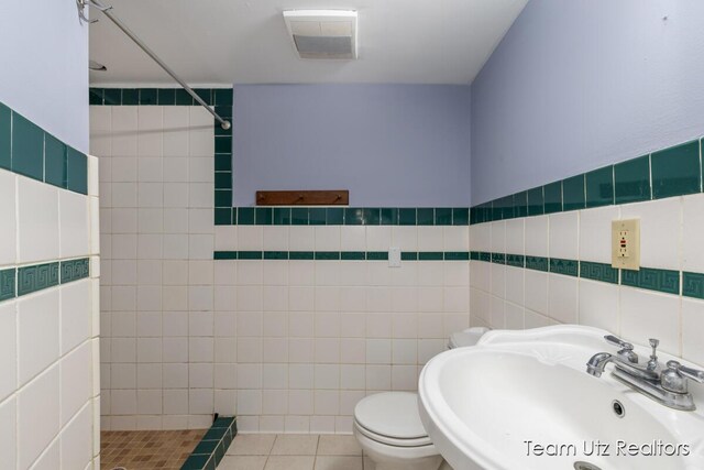bathroom with a tile shower, a sink, toilet, tile patterned floors, and tile walls