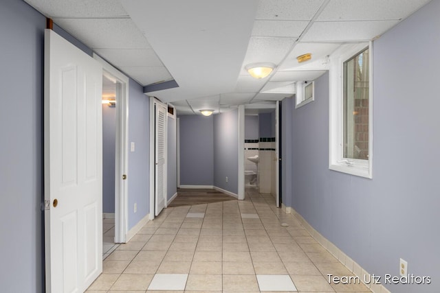 corridor with light tile patterned flooring, baseboards, and a paneled ceiling