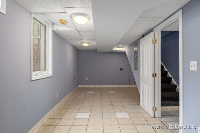 finished below grade area with baseboards, a drop ceiling, light tile patterned floors, and stairway