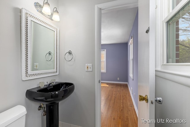 half bath with baseboards, wood finished floors, and toilet