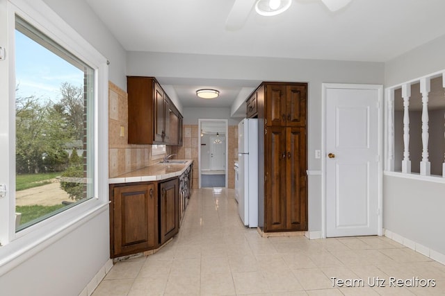 kitchen featuring dark brown cabinets, ceiling fan, a sink, freestanding refrigerator, and baseboards