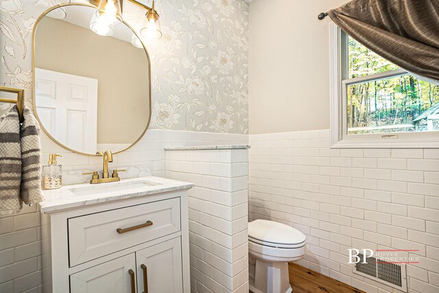 bathroom featuring vanity, wainscoting, toilet, tile walls, and wallpapered walls