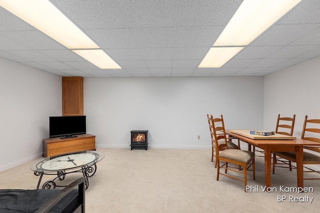 carpeted dining space featuring baseboards, a wood stove, and a paneled ceiling
