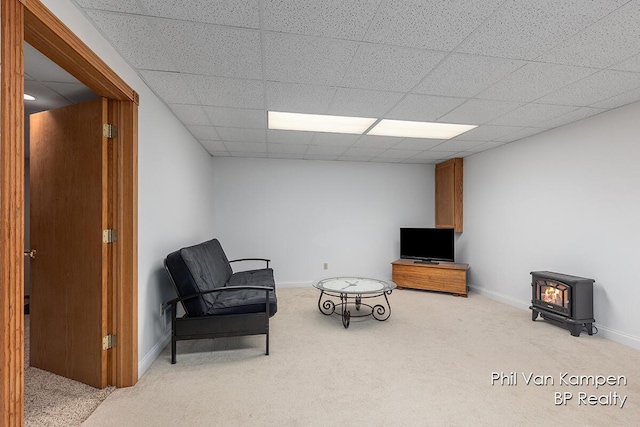 sitting room with carpet floors, baseboards, a wood stove, and a paneled ceiling