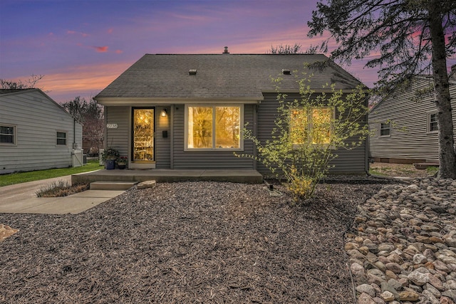 back of property at dusk featuring roof with shingles