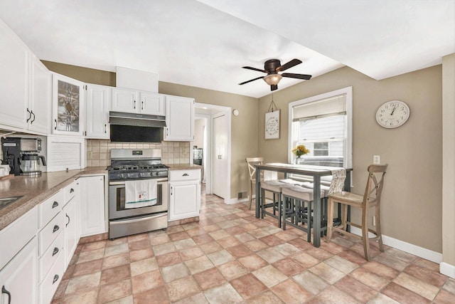 kitchen featuring baseboards, decorative backsplash, white cabinets, and gas stove