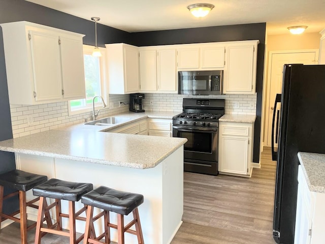 kitchen with decorative backsplash, a peninsula, a sink, light wood finished floors, and black appliances