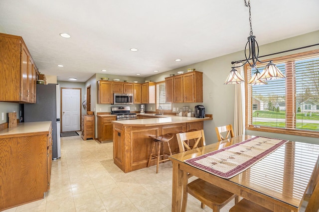 kitchen with brown cabinets, appliances with stainless steel finishes, a sink, light countertops, and a peninsula