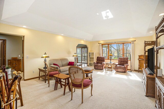 living area with arched walkways, baseboards, light carpet, and a raised ceiling