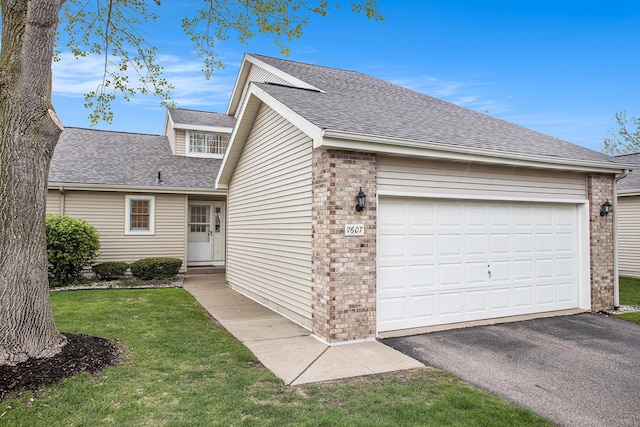 view of front of home with an attached garage, a shingled roof, brick siding, a front yard, and driveway