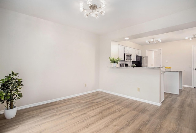 kitchen featuring stainless steel appliances, a notable chandelier, a peninsula, and light wood-style floors