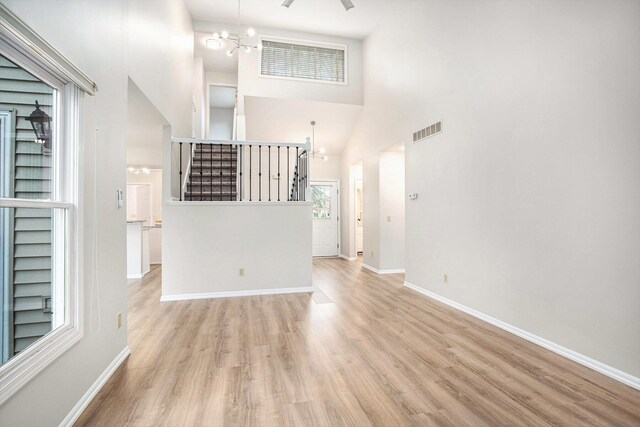 unfurnished living room with wood finished floors, a high ceiling, a chandelier, and visible vents
