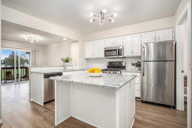 kitchen featuring appliances with stainless steel finishes, tasteful backsplash, a sink, a peninsula, and a notable chandelier