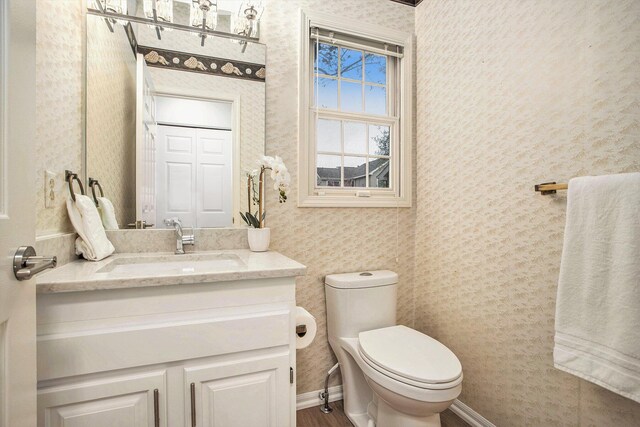 bathroom with vanity, toilet, wallpapered walls, and wood finished floors