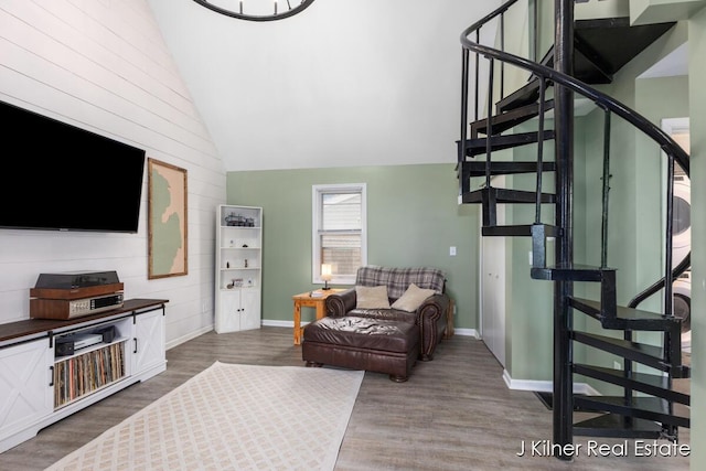 living area featuring wood finished floors, lofted ceiling, baseboards, wooden walls, and stairway