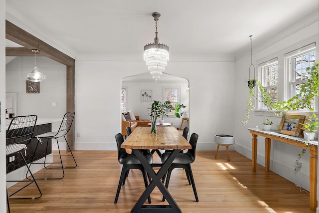 dining area featuring arched walkways, baseboards, a notable chandelier, and light wood-type flooring