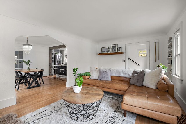 living area with arched walkways, baseboards, an inviting chandelier, and light wood-style flooring