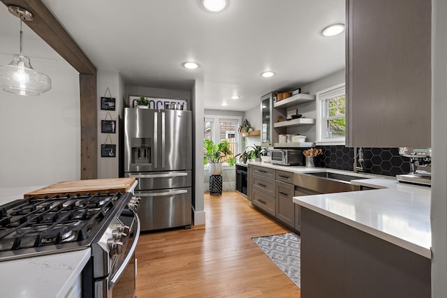 kitchen featuring appliances with stainless steel finishes, open shelves, a sink, light countertops, and a wealth of natural light