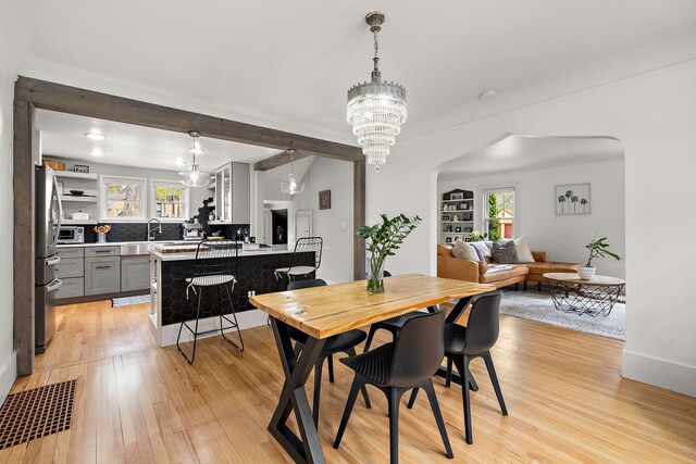 dining space with arched walkways, beam ceiling, baseboards, a chandelier, and light wood-style flooring