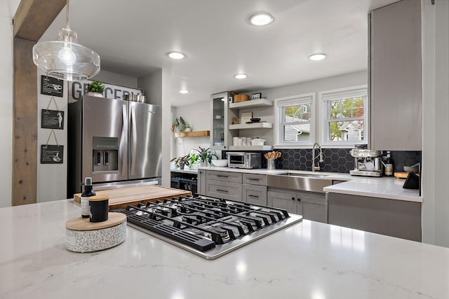 kitchen with light stone countertops, gas cooktop, stainless steel fridge, a sink, and gray cabinets