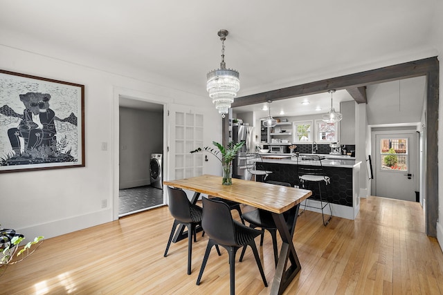 dining area with light wood-style floors, baseboards, washer / dryer, and beam ceiling