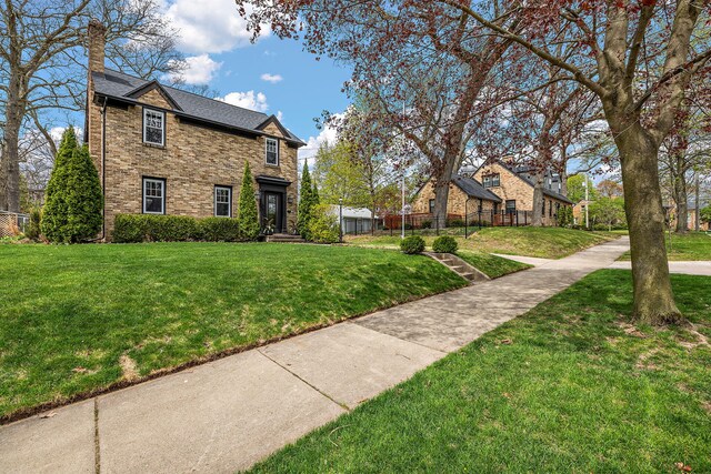 traditional home with fence, a chimney, brick siding, and a front yard