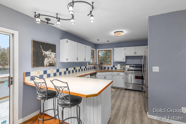 4600 S Teal Ln, Newaygo, MI 49337 - kitchen with white cabinets, a sink, stainless steel appliances, a peninsula, and light wood-type flooring