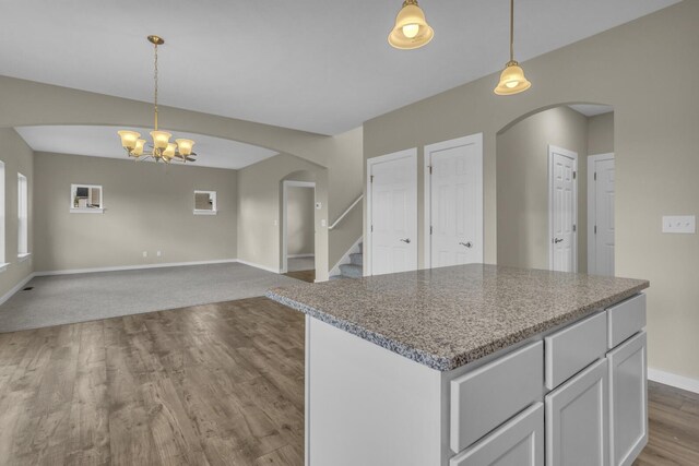kitchen with pendant lighting, wood finished floors, baseboards, a chandelier, and arched walkways