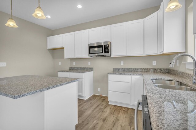 kitchen with white cabinets, a sink, light wood-style flooring, stainless steel microwave, and pendant lighting