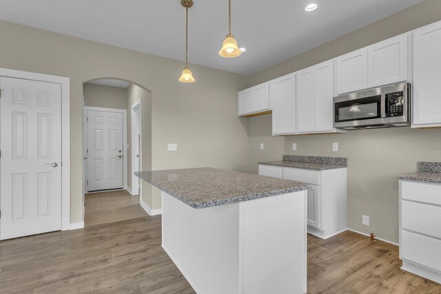 kitchen with arched walkways, white cabinets, stainless steel microwave, and light wood-style flooring