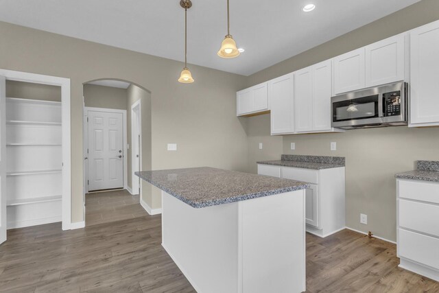 kitchen with arched walkways, white cabinets, stainless steel microwave, and wood finished floors