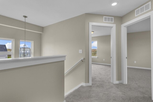 hallway featuring baseboards, visible vents, carpet, and an upstairs landing